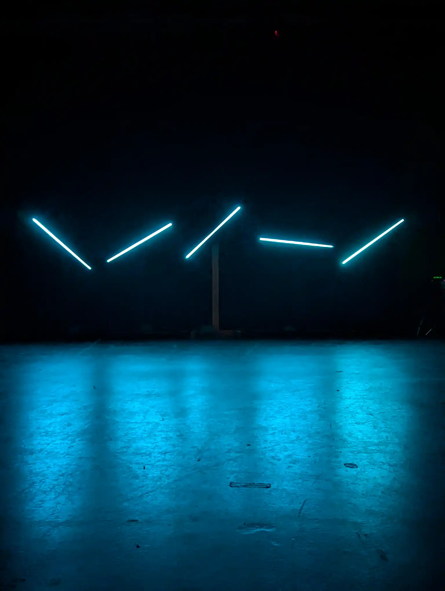 Salle plongée dans le noir avec cinq bâtons lumineux au fond